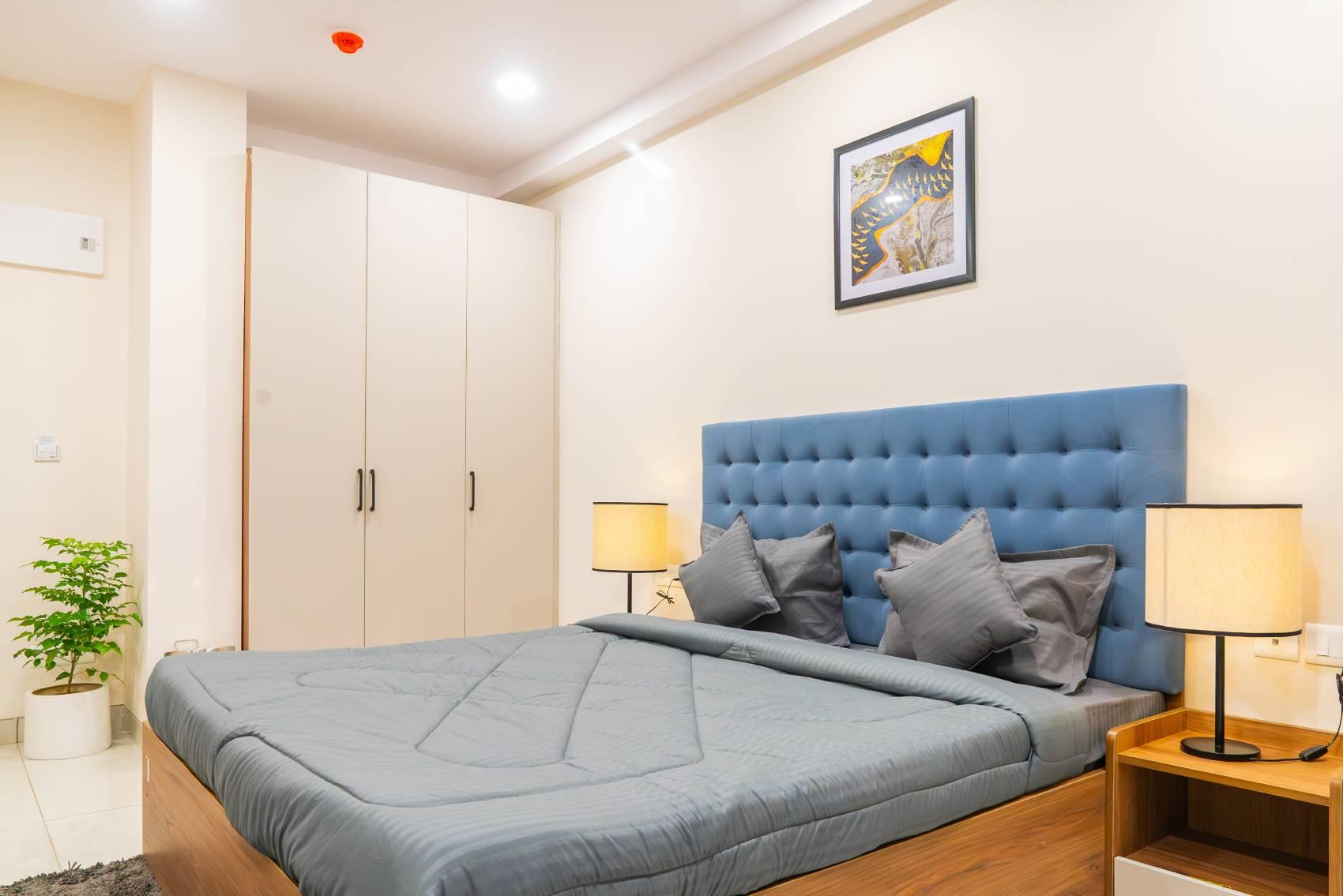 Modern studio room for rent in Kondapur featuring a double bed with a blue tufted headboard, bedside lamps, and a spacious built-in wardrobe.